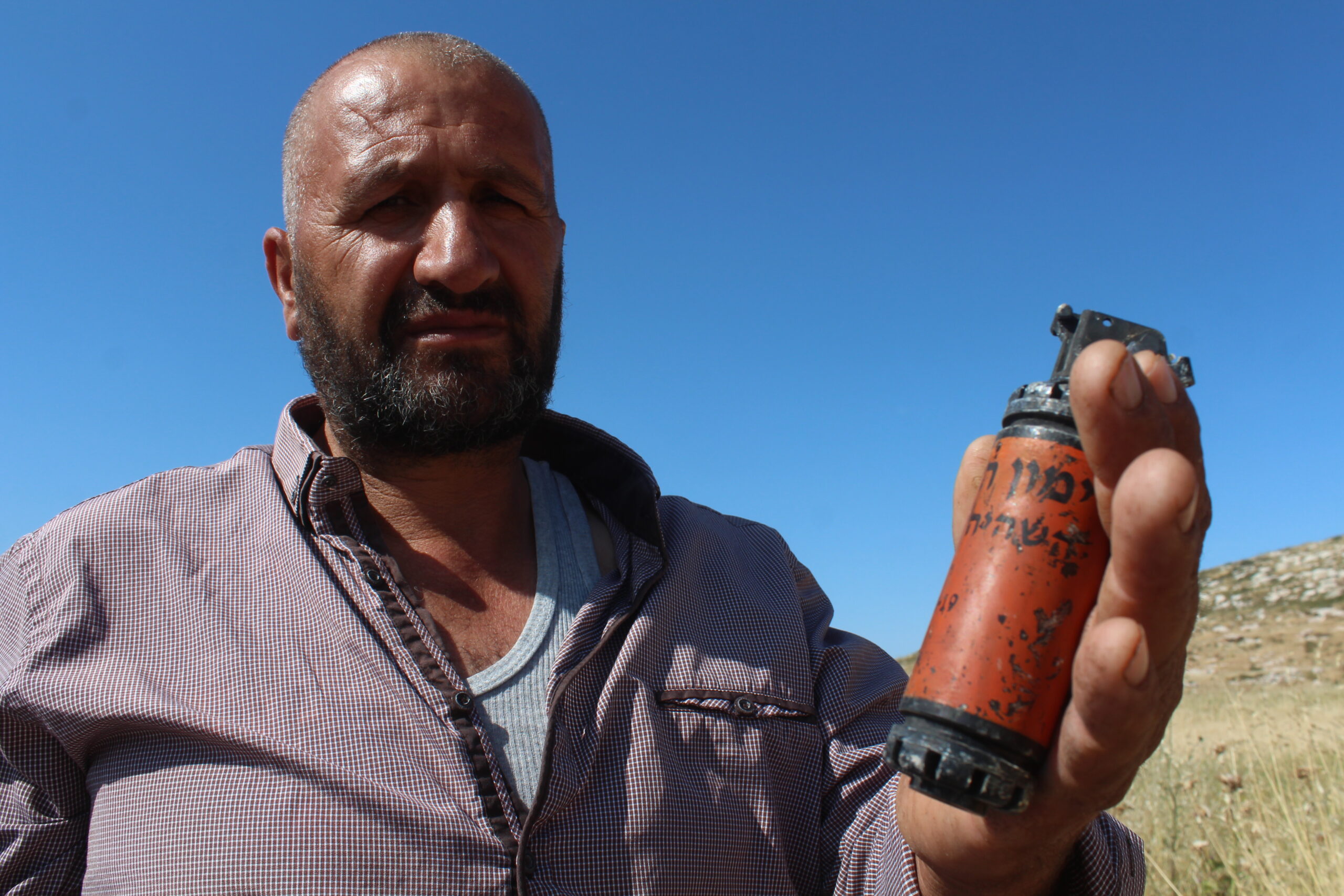 عودة يحمل واحدة من بقايا قنابل الغاز الذي أطلقها جيش الاحتلال باتجاه المزارعين، وجدها في أرضه. (عدسة: شذى حمّاد).