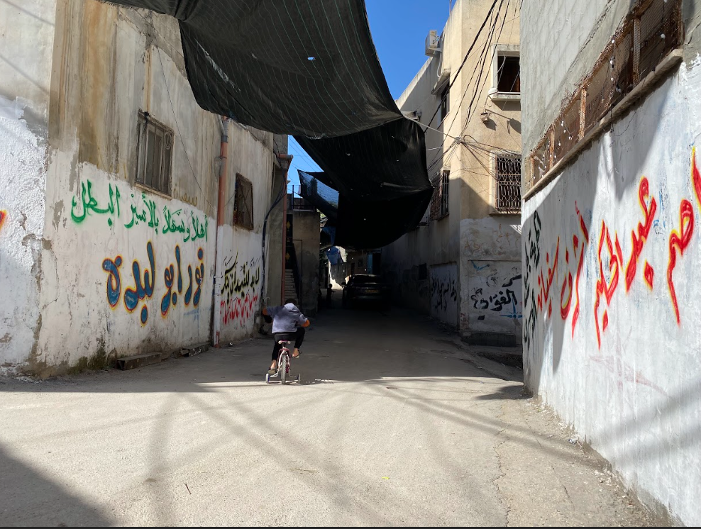 أحد أزقة مخيم نور شمس، وتبدو "الشوادر" تمتد فوقه لتحجب مراقبة الطائرات الإسرائيلية. عدسة: شذى حمّاد.